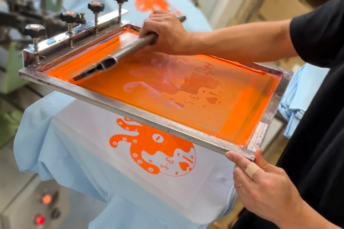 シルクスクリーンプリントの版にインクを乗せてTシャツに刷る作業